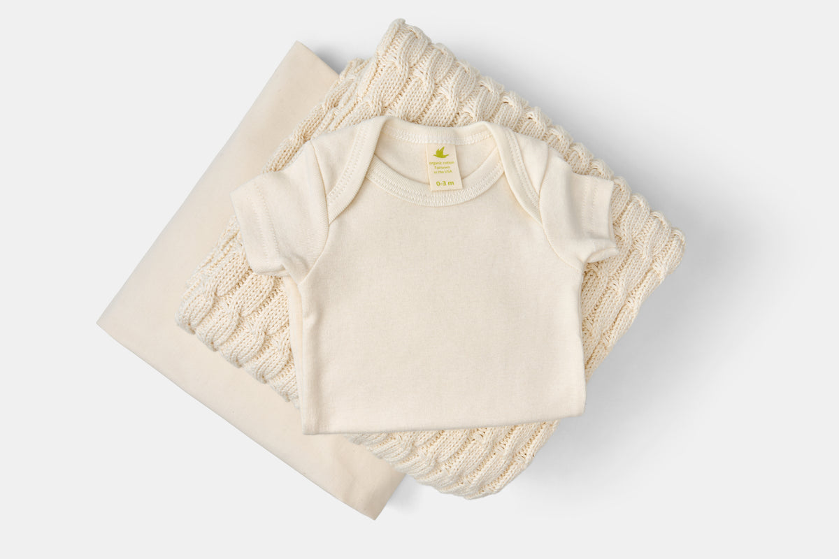 Baby clothing bundle with cream-colored onesie, knitted blanket, and fabric