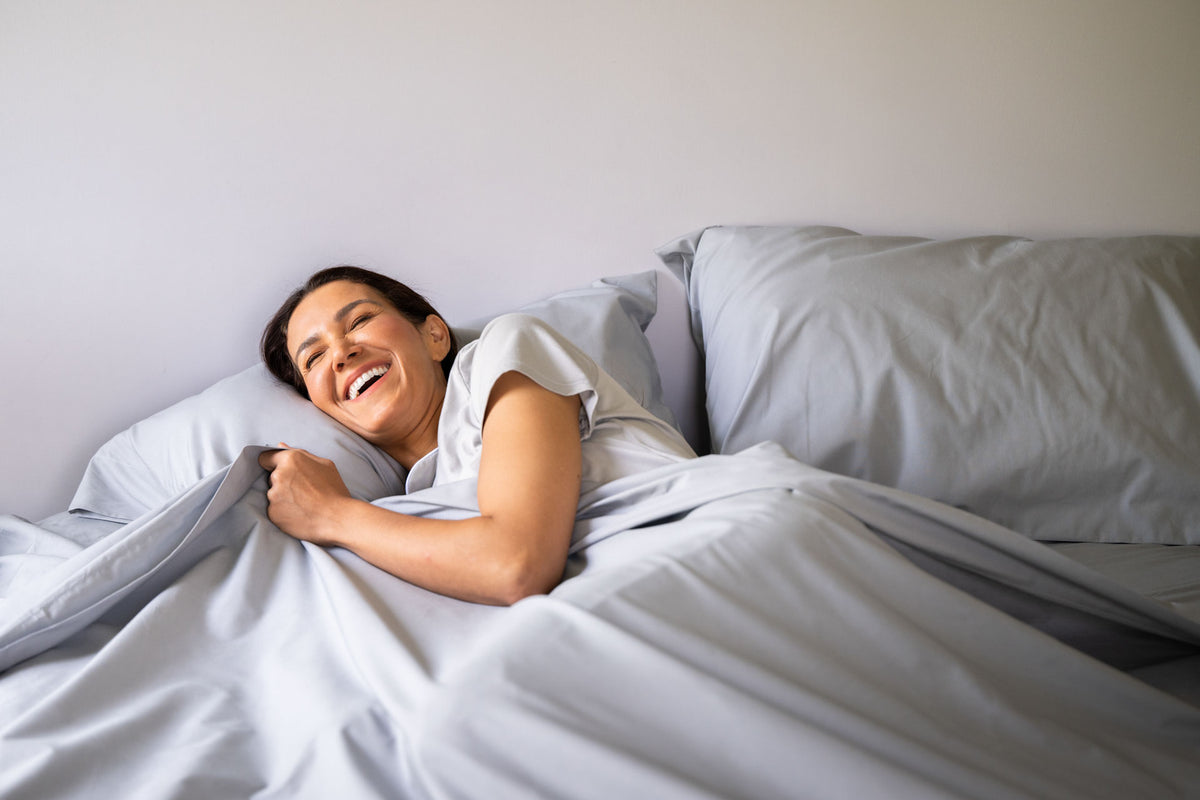 Smiling woman relaxing on bed with light gray cotton percale sheets