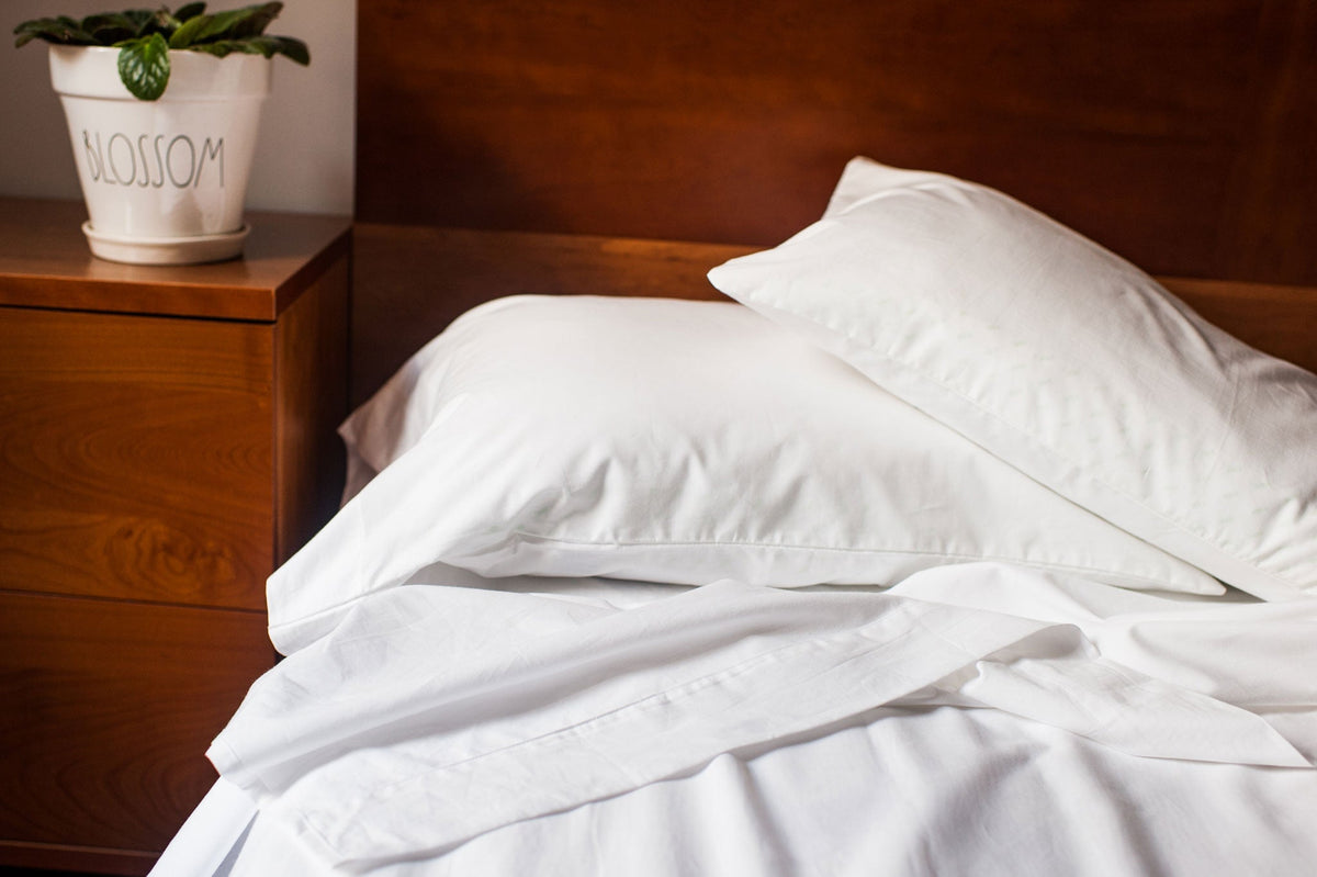 White fitted bed sheet with pillow on wooden bed