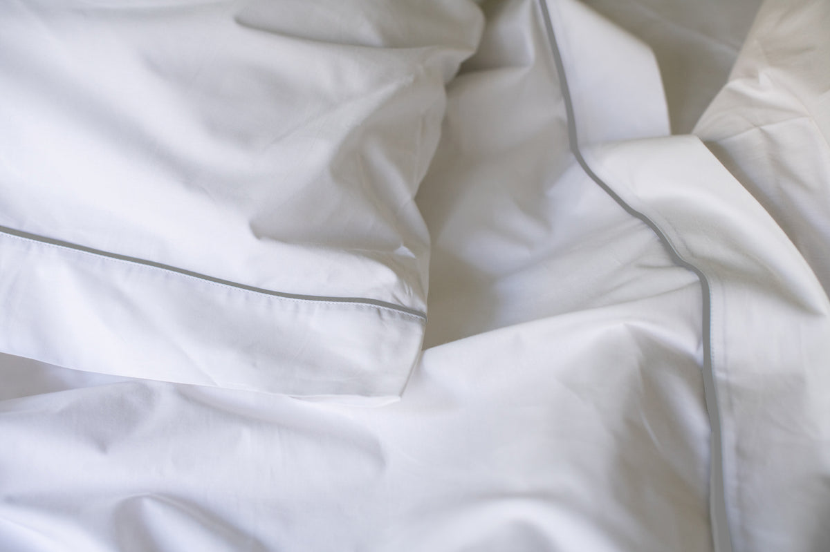 Close-up of white cotton bed sheet with piping detail, crumpled for texture
