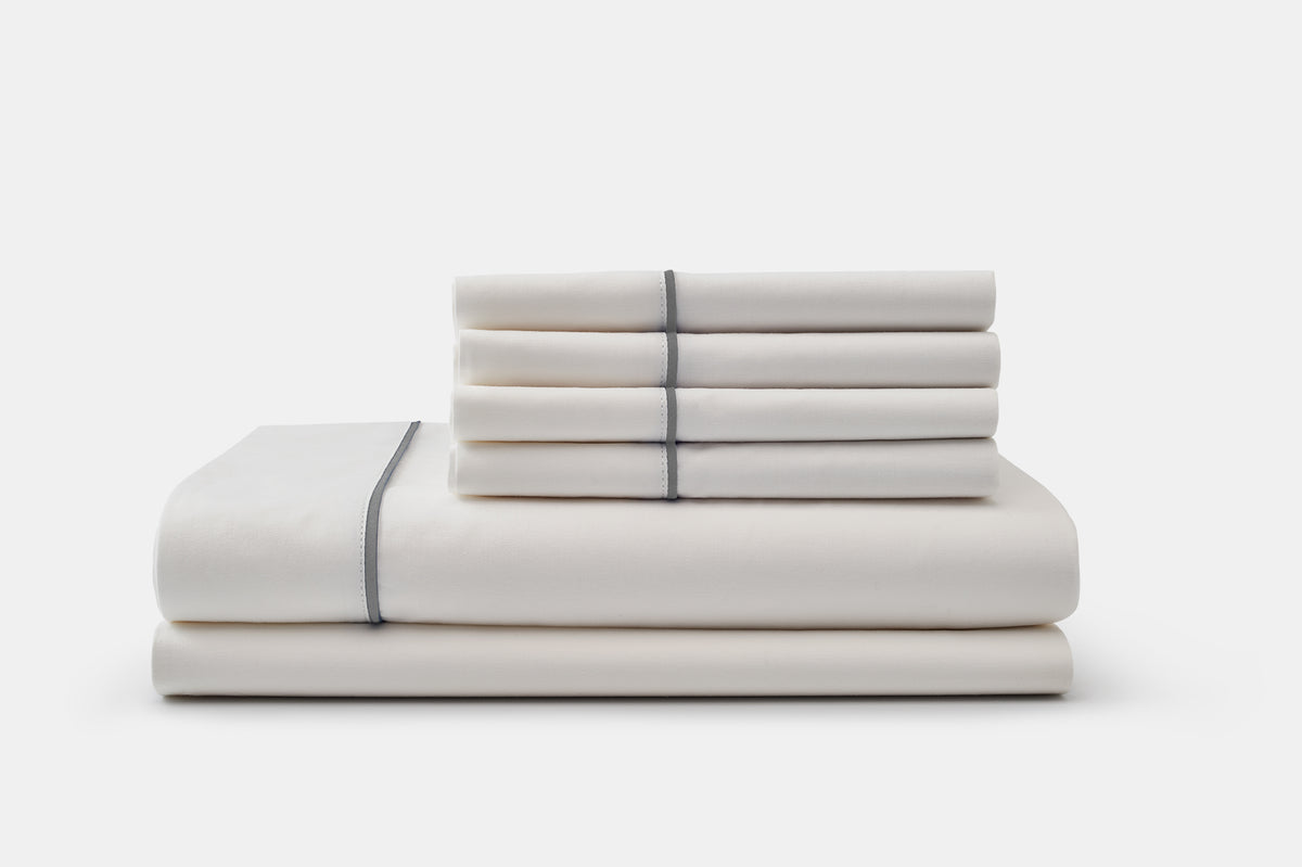 White cotton bed sheet set with classic piping design, neatly folded